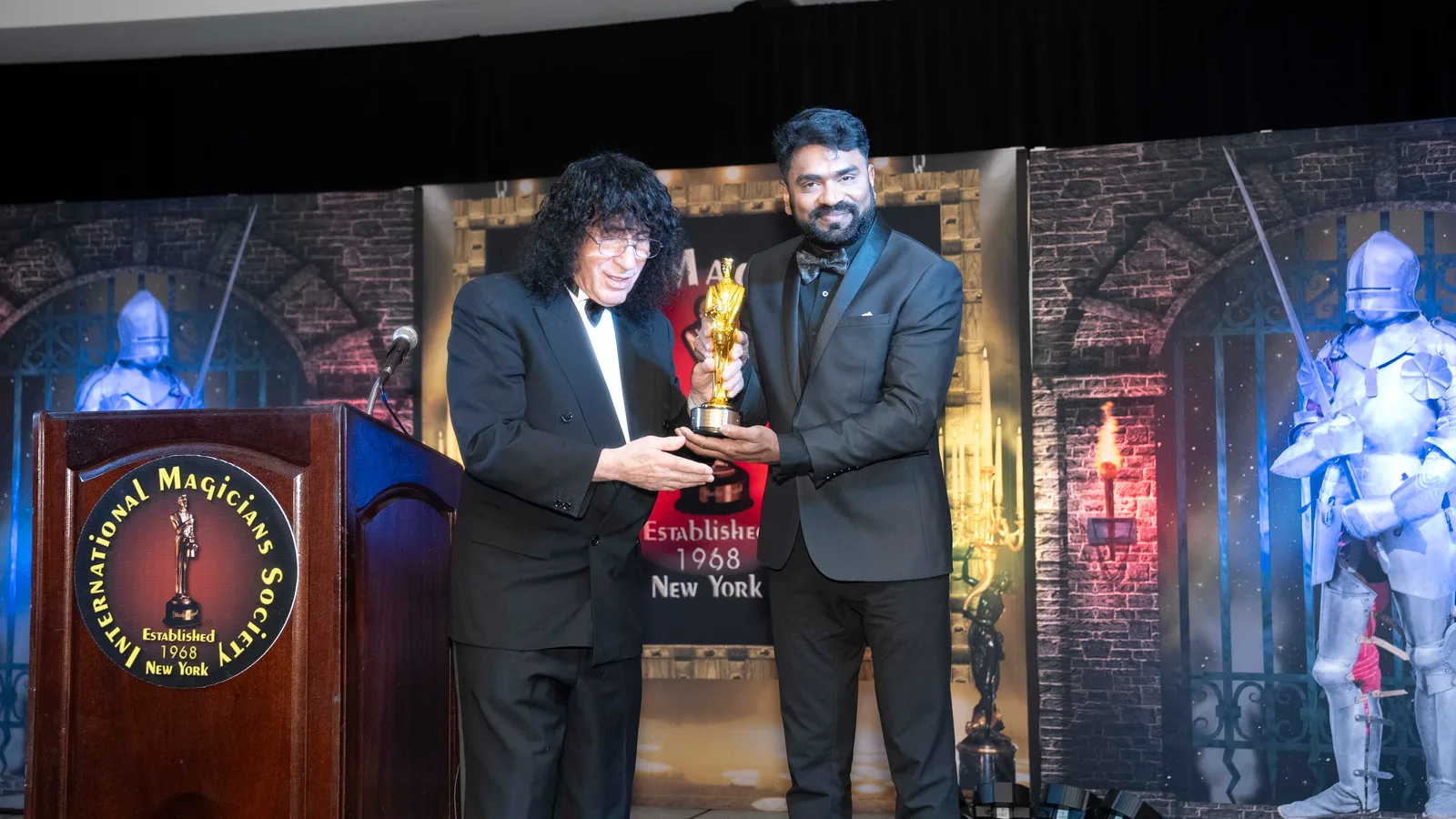 Tony Hassini and Aravind V.K. holding the Merlin Award together on stage